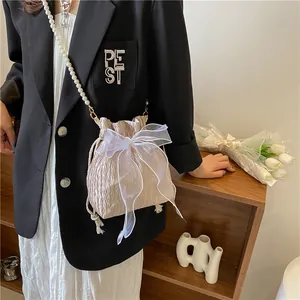 Close-up of champagne pleated bucket bag with large white organza bow and pearl strap