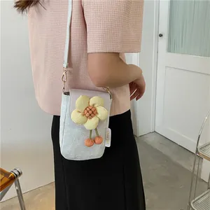 Close-up of a white embossed crossbody phone bag with a large 3D yellow flower and pom-poms