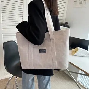 Detail of grey canvas tote bag featuring a front pocket and FASHION label patch