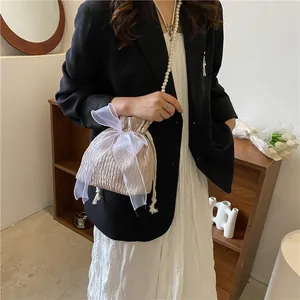 Detail of champagne pleated bucket bag featuring an organza bow and pearl shoulder strap
