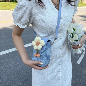 Detail of light blue floral phone bag featuring a 3D cream petal charm and orange tassel
