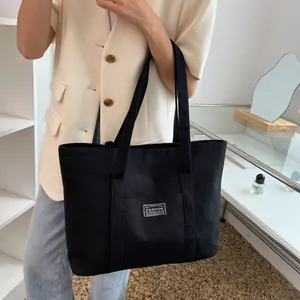Detail of black canvas tote bag showing the reinforced shoulder straps and fashion logo