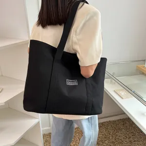 Rear view of a model wearing a large black canvas tote bag in a modern interior setting