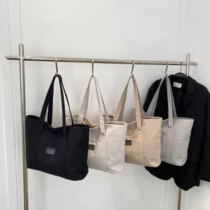 Detail view of four minimalist canvas tote bags in black, white, beige and grey hung on a rack