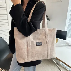 Minimalist beige canvas tote bag with fashion label shown in a lifestyle office setting