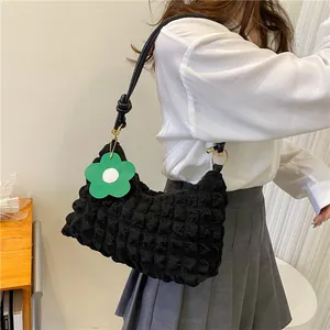 Gros plan d'un sac à bandoulière plissé noir avec texture gaufrée et charm fleur verte