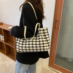 Gros plan d'un grand sac cabas à carreaux avec bandoulières en cuir crème porté à l'épaule