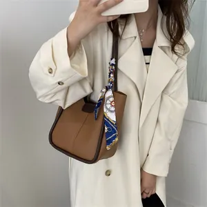 Gros plan d'un sac seau marron avec foulard décoratif à la main tenu par un modèle