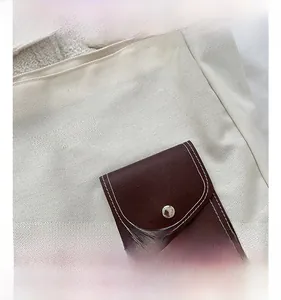 Detail of canvas tote featuring a brown leather pocket with silver button and contrast stitching