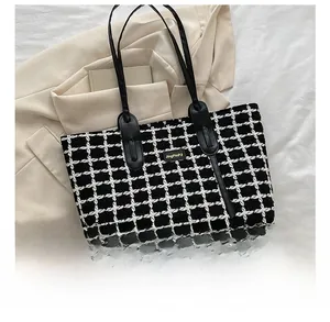 Détail d'un sac cabas à carreaux noir et blanc avec logo doré sur fond de veste beige
