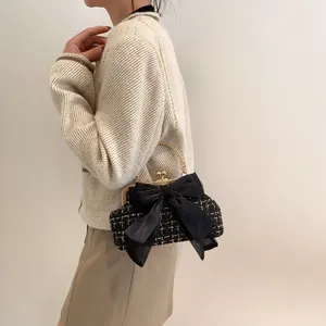 Detail of tweed crossbody bag featuring black satin bow and golden chain strap
