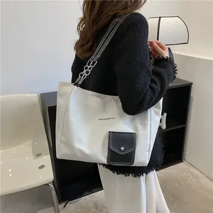 Detail of canvas tote bag showing contrast pocket and metal chain leather shoulder strap