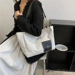 Detail of canvas tote bag showing black PU pocket, metal clasp, and chain shoulder strap