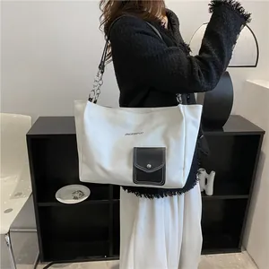 Detail of canvas tote bag showing black leather pocket and chain shoulder strap design