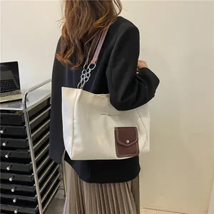 Detail of white canvas tote bag with a small brown leather pocket and metal chain strap