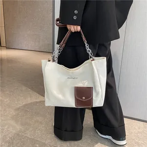Close-up of white canvas tote bag with brown leather pocket and metal chain strap details