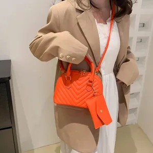 Schicke orangefarbene gesteppte Muschel-Handtasche mit Mini-Geldbörse an einem Modell