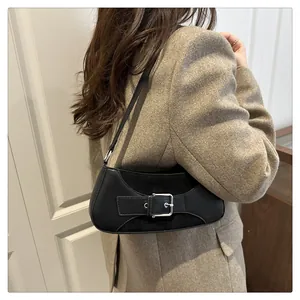 Detalle de un bolso de hombro en cuero negro con hebilla plateada en una modelo