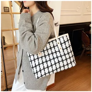 Close-up of houndstooth tote bag with white leather straps and golden rivet details