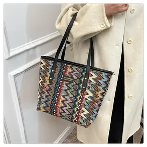 Nahaufnahme einer bunten Zickzack-Webtasche mit Lederriemen auf einem beigen Wollmantel