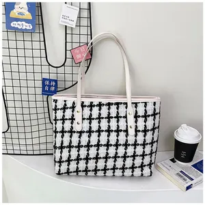 Detail of checkered woven tote bag featuring leather handles and metal rivet fasteners