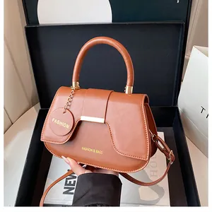 Détail du sac selle marron avec boucle dorée et breloque dans son coffret de luxe