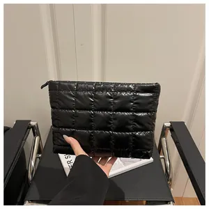 Close-up of a model holding a black quilted glossy nylon makeup bag with zipper detail