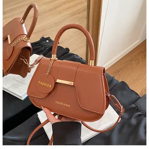 Vue détaillée du sac besace en cuir marron avec barre métallique dorée et pendentif