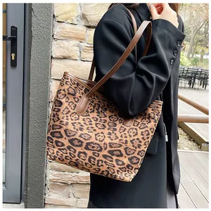 Dettaglio di una borsa tote leopardata con manici in pelle marrone indossata a spalla da donna