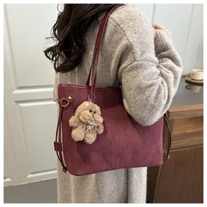 Detail of burgundy suede tote bag with drawstring and cute plush dog charm on a model