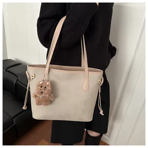 Detail of beige tote bag with slim shoulder straps and cute plush dog charm accessory