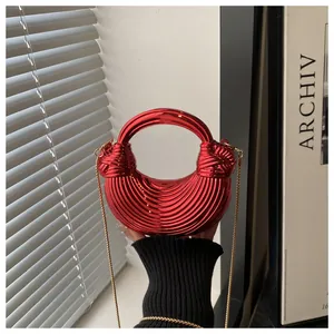 Dettaglio borsa a mezzaluna rosso metallizzato con trama a onde, manico e catena oro