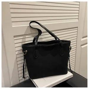 Detail of black matte tote bag with polished leather trim and gold metal hardware