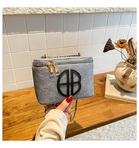 Détail du sac à main gris texturé avec fermetures dorées et logo métallique circulaire