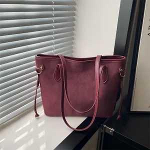 Large burgundy red suede tote bag with drawstring details and gold hardware in natural light