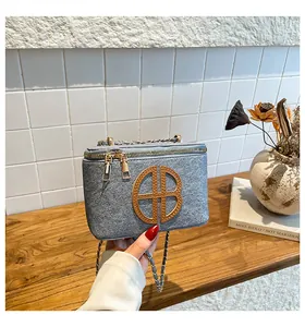 Détail du sac boîte en denim bleu avec boucle logo dorée et bandoulière en chaîne