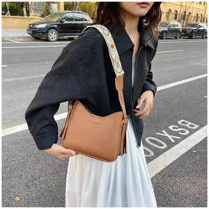 Brown leather crossbody bag with wide floral strap shown in an outdoor street scene