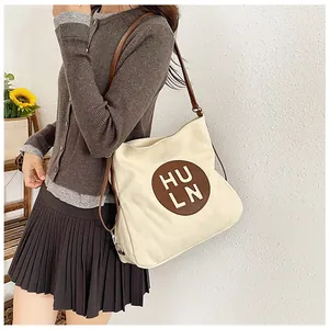 Detail of the HULN logo patch and adjustable brown strap on a cream canvas tote bag