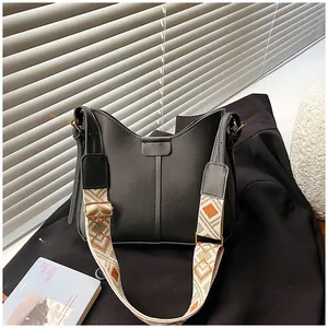 Detail of wide woven strap with geometric pattern on a minimalist black shoulder bag