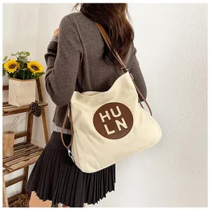 Close-up of beige canvas tote bag featuring brown leather logo patch and shoulder straps