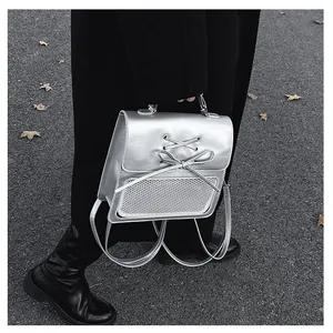 Silver metallic backpack with lace-up bow and mesh pocket shown in an outdoor street setting
