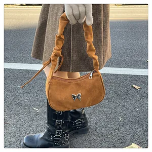 Close-up of brown suede shoulder bag featuring a silver butterfly buckle and ruched strap