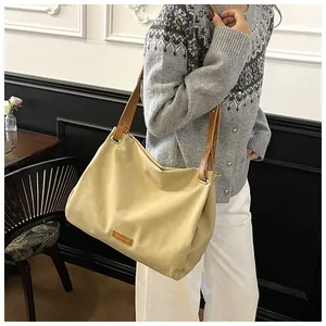 Detail of a beige canvas tote bag with brown leather straps and vintage metallic rivets