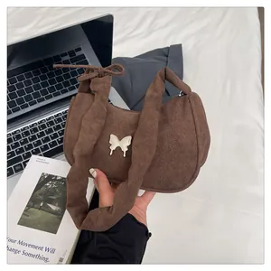 Detailed macro of a brown suede crescent bag featuring a silver metal butterfly ornament