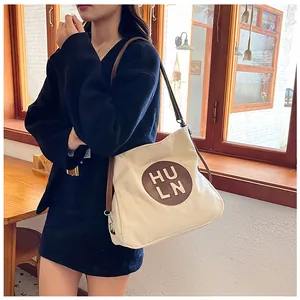Detail of off-white tote bag with brown circular logo patch and long leather straps