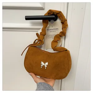 Detailed view of brown suede underarm bag with silver butterfly and ruffled strap