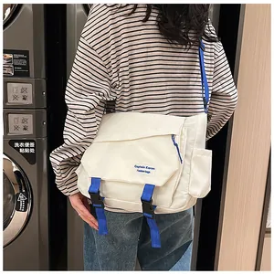 White canvas messenger bag with blue straps and buckle detail shown in a laundry room setting