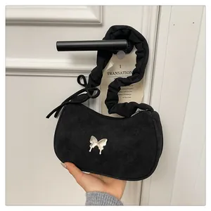 Macro detail of suede crescent bag featuring liquid metal butterfly and ruched handle strap