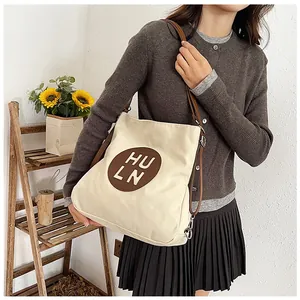Detail of canvas tote bag with adjustable brown leather strap and decorative logo patch