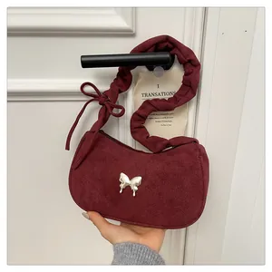 Detail of burgundy suede shoulder bag featuring a silver butterfly charm and pleated strap
